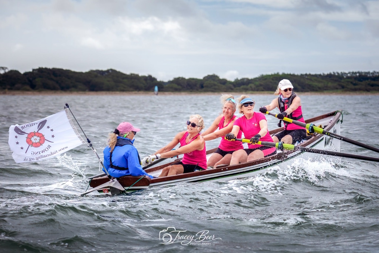 A crew rowing a wooden boat through choppy harbour water.